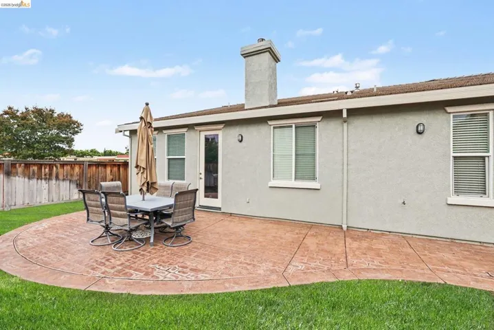 Expansive backyard featuring a curved stamped concrete patio, a stucco exterior, and a manicured lawn