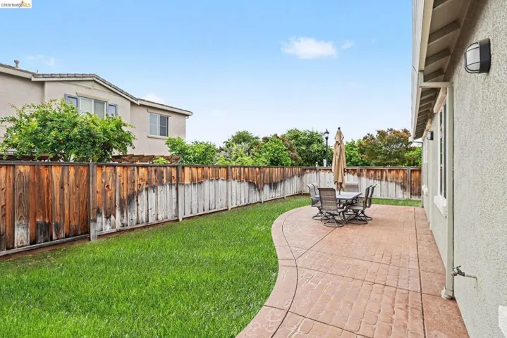 Expansive backyard featuring a concrete patio with stamped brick pattern, a manicured lawn, and a wood fence border