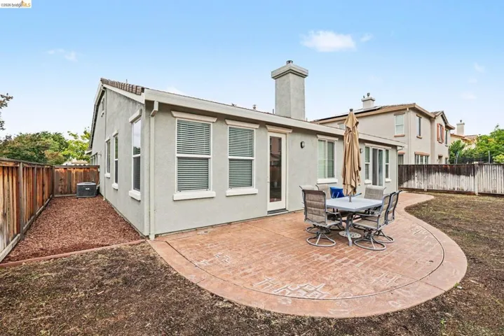 Exterior patio featuring stamped concrete, stucco siding, multiple windows with blinds, a glass-paneled door, and a chimney structure
