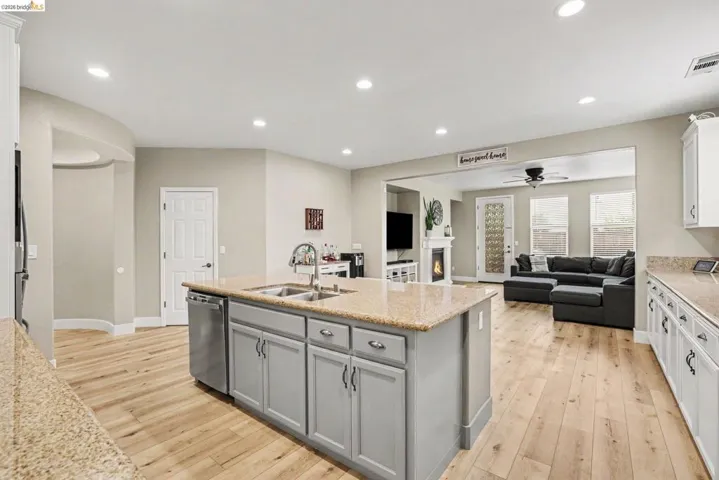 Open-concept kitchen and living area featuring wood-finish flooring, recessed lighting, a kitchen island with sink and stainless steel dishwasher, and light-toned countertops
