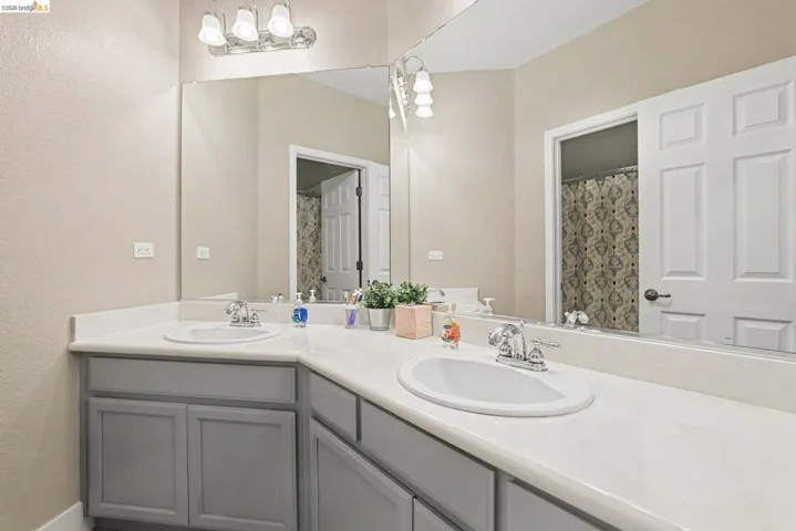 Double vanity featuring two integrated sinks set into a light-toned countertop, gray cabinetry, and a full-width mirror