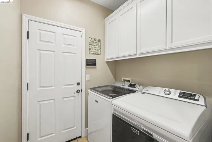 Dedicated laundry area featuring overhead white cabinetry with shaker-style doors, light-toned walls, and a white paneled door with dark hardware