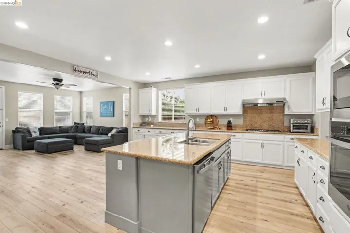Kitchen featuring white cabinetry, light-toned countertops, stainless steel appliances, and a central island with a double sink