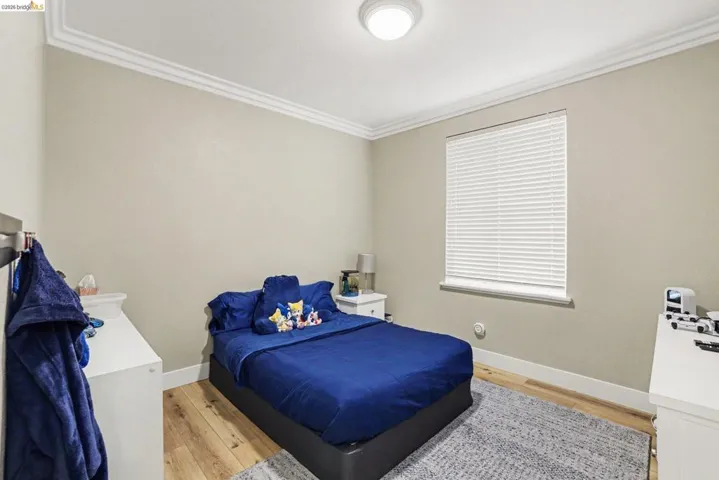Bedroom with wood-finish flooring, crown molding, and a single window with blinds