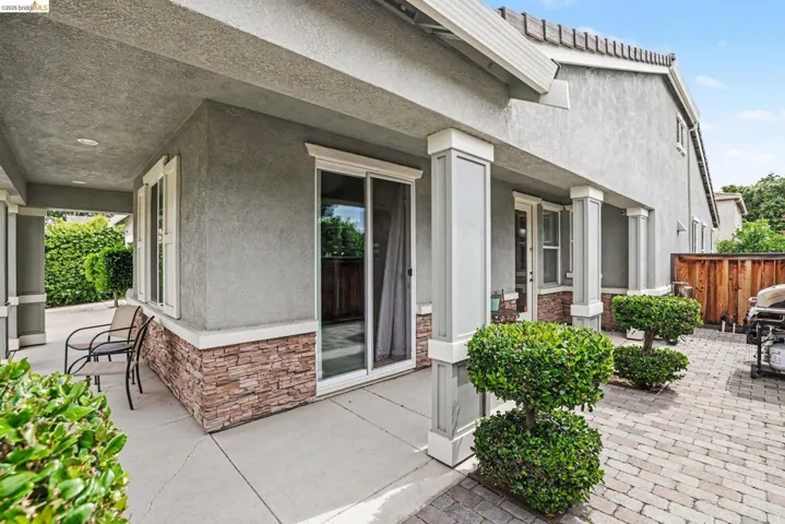 Covered patio featuring a stucco exterior with stone veneer accents, white trim, and a sliding glass door