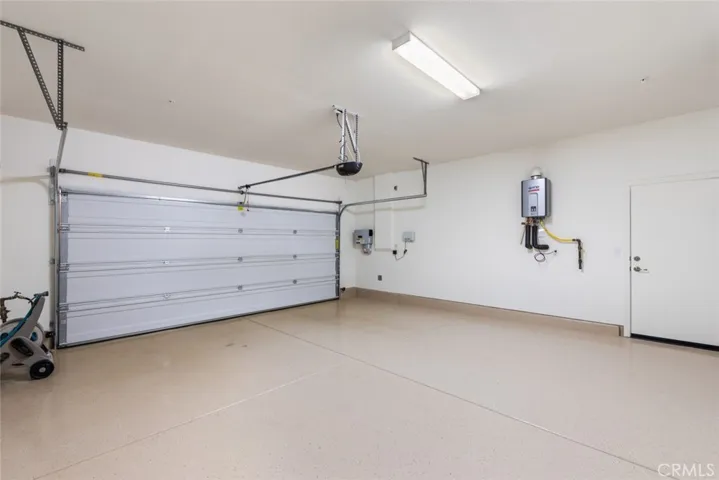 Fully Drywalled Two Car Garage with Epoxy Floors, showing the Solar System Inverter, the Sprinkler System Control Panel, the Tankless WH and the Garage Service Door to the SideYard.