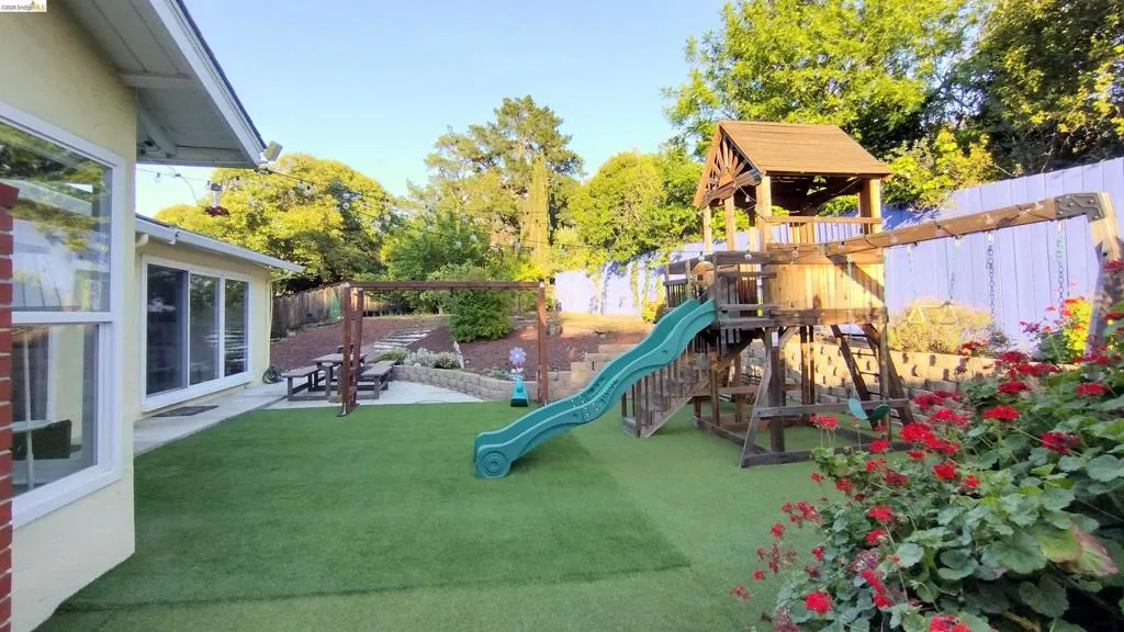 View of playground with a fenced backyard and a patio area