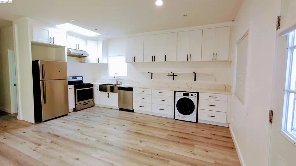 ADU living room/Kitchen combo, featuring washer / clothes dryer, white cabinetry, stainless steel appliances, light wood finished floors, and recessed lighting