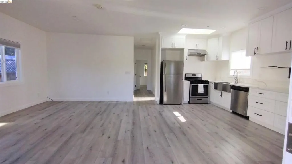 Kitchen featuring white cabinetry, stainless steel appliances, light wood-style flooring, open floor plan, and light stone counters