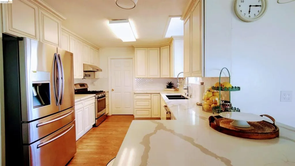 Kitchen with stainless steel appliances, light wood-type flooring, backsplash, light stone counters, and white cabinetry