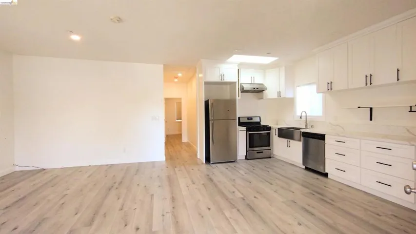Kitchen with stainless steel appliances, white cabinets, light wood finished floors, and light stone counters