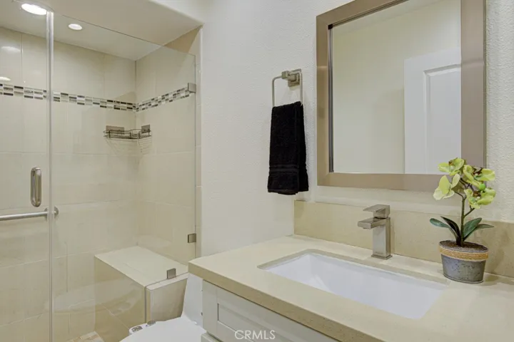 Pretty upgraded bathroom features a step in shower and bench and glass enclosure. The under-mount sink is topped with a neutral quartz countertop.