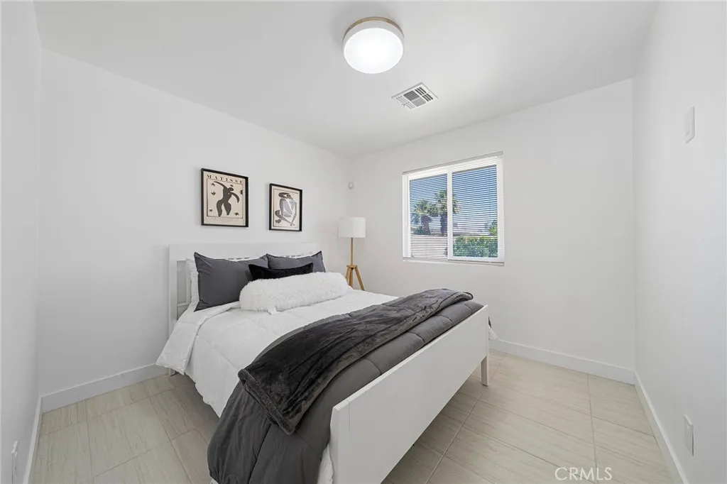 Bedroom at the front end corner of the home with tile flooring, double pane window and view of the front yard. Furniture remains.