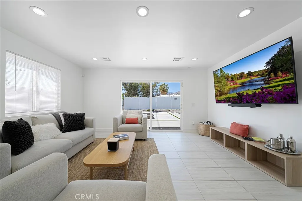 Living room with tile flooring, recessed lighting, double pane window and slider. Furniture remains. Art on wall is excluded.