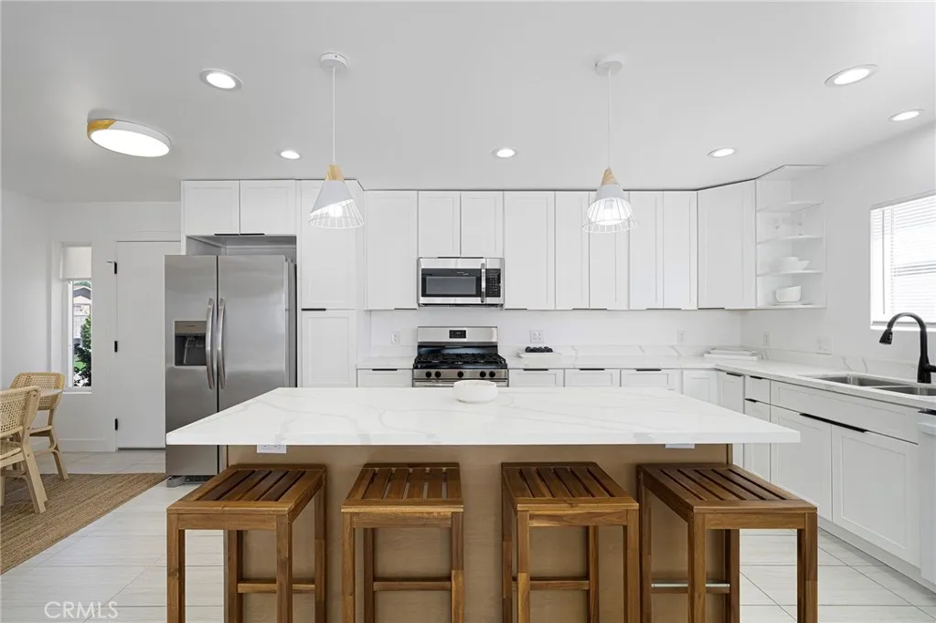 Spacious updated kitchen with recessed lighting and roomy island with quartz counters. Appliances and items in  cabinets remain along with the stools. Plugs under island counter for your use of other kitchen items or plug in your devices. Window view of side yard from kitchen sink. Dining area to the left. Door by refrigerator leads to the laundry and door to garage. Skinny window from dining has the view of the front.