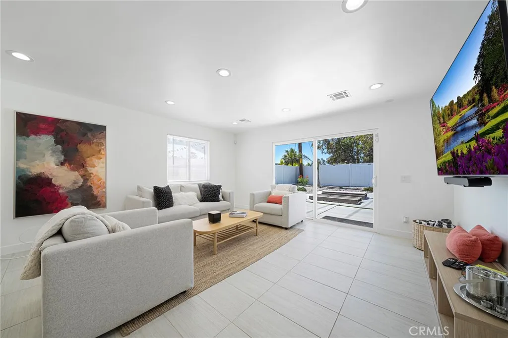 Living room with tile flooring, recessed lighting, double pane window and slider. Furniture remains. Art on wall is excluded.