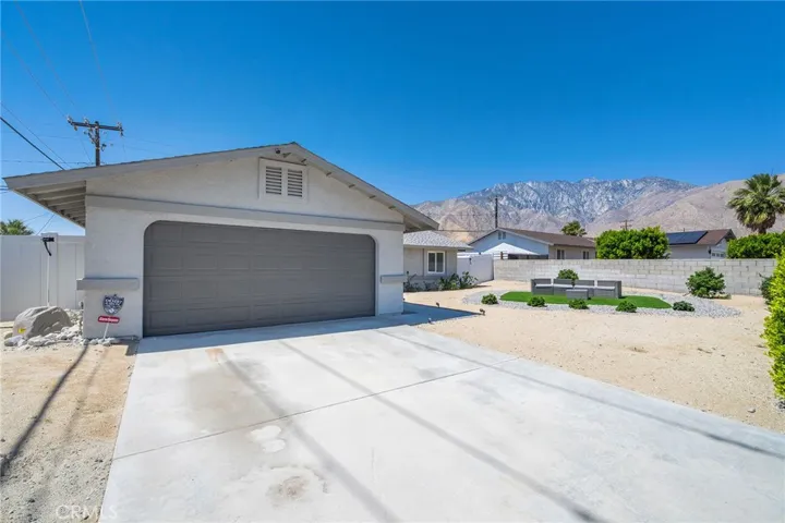 Two car garage and room for two in the driveway. Roomy frontward with turf and rock island. Furniture remains. View of San Jacinto mountains. Vinyl and block wall fencing.