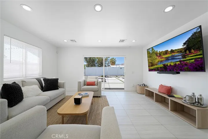 Living room with tile flooring, recessed lighting, double pane window and slider. Furniture remains. Art on wall is excluded.