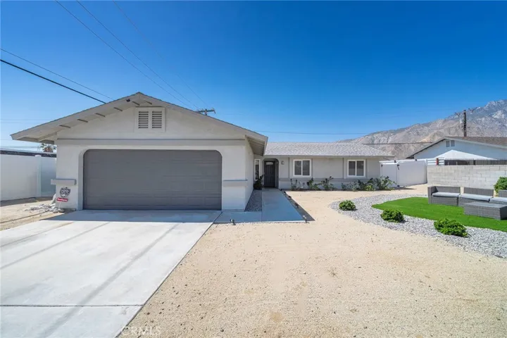 Two car garage and room for two in the driveway. Roomy frontward with turf and rock island. Furniture remains. View of San Jacinto mountains.