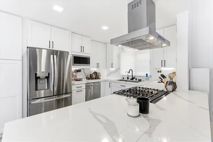 Modern kitchen with island and breakfast bar, stainless steel appliances, and open sightlines to the living area and staircase