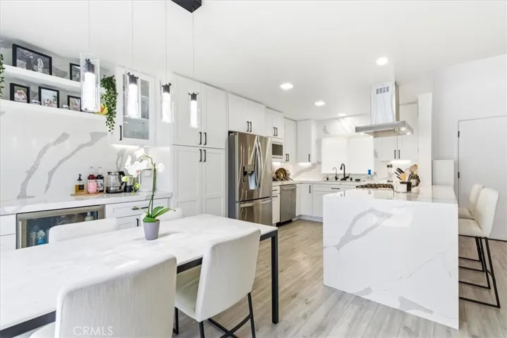Modern open kitchen and dining area with marble surfaces, stainless steel appliances, and breakfast bar, captured from a wide-angle corner view.
