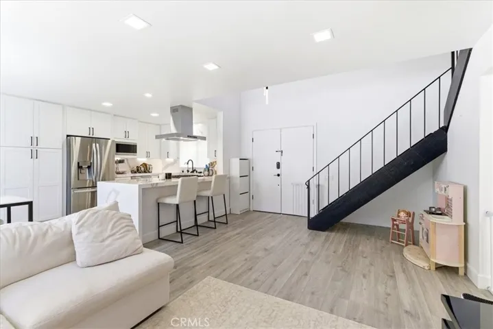 Bright open living space with white sectional, modern staircase, and open-concept kitchen with stainless steel appliances.