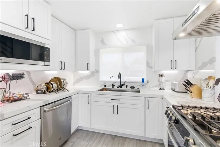 Bright open-concept kitchen and dining space with white cabinetry, marble countertops, and stainless steel appliances, viewed from the corner angle.