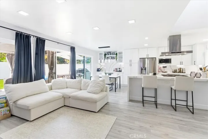 Wide-angle interior shot from the living room corner showcasing the open-concept space, white sectional sofa, modern kitchen with breakfast bar, and sliding doors leading to the backyard.