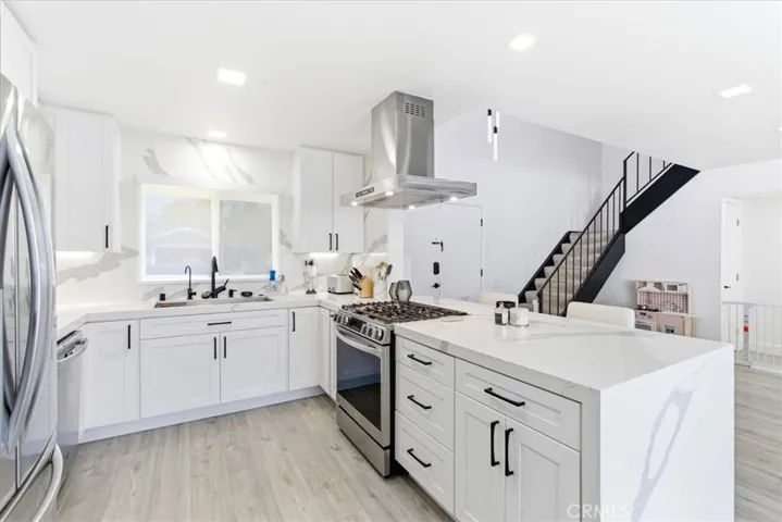 Modern kitchen with white cabinetry, marble countertops, stainless steel appliances, and an island with breakfast bar, captured in a wide-angle view including the staircase and open living space.