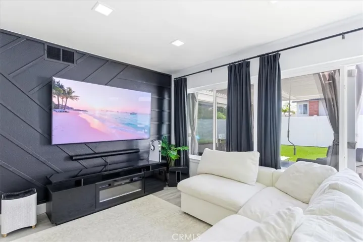 Bright living room with a modern black accent wall, wall-mounted TV, white sectional sofa, and large sliding doors opening to the backyard, allowing abundant natural light.