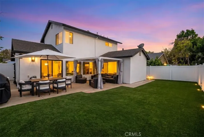 Twilight backyard view highlighting patio lighting and landscaped lawn.