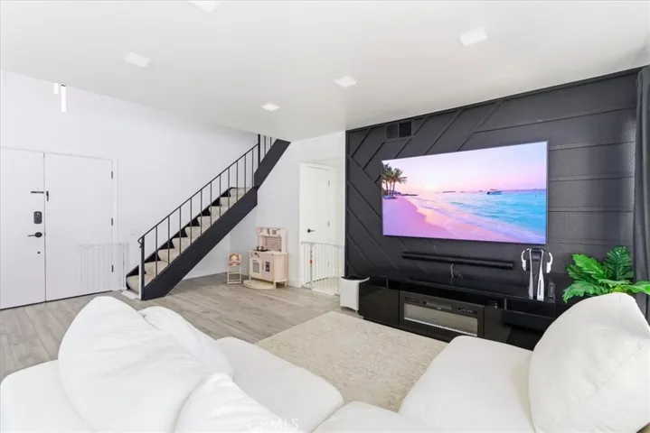 Spacious living area with modern black accent wall, wall-mounted TV, white sectional sofa, and staircase leading to the upper level, with large windows providing natural light and a view of the backyard.