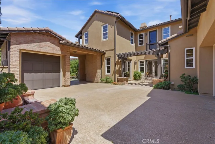 A private courtyard garage entrance framed by classic Monterey Colonial architecture, brick accents, and a pergola-covered courtyard creates a warm and welcoming arrival experience.