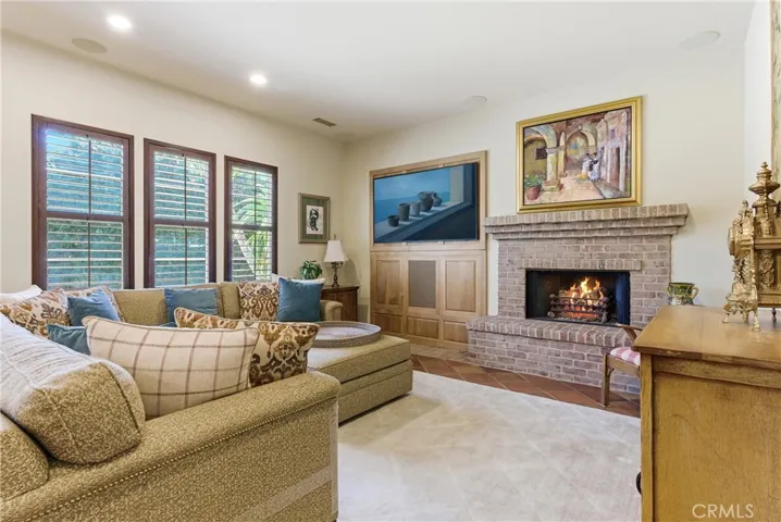 The inviting family room showcases a custom built-in media center, plantation shutters, and a stunning brick fireplace that serves as the heart of the home.
