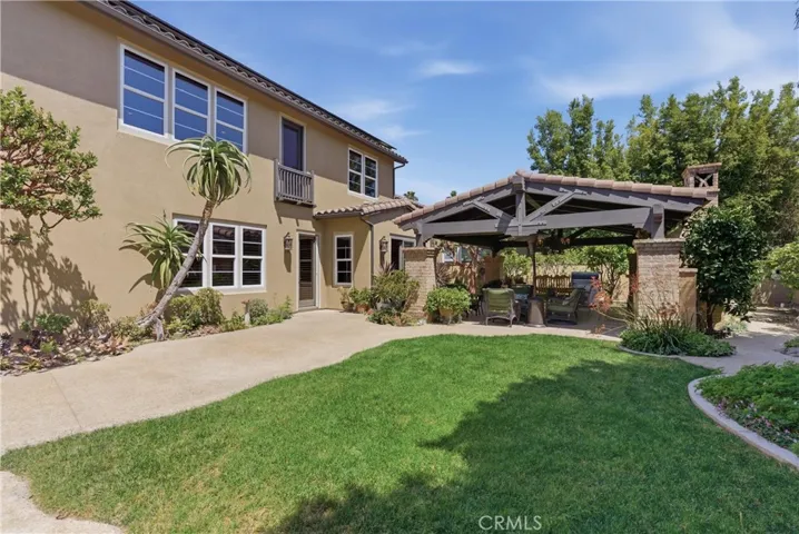 Backyard perspective showcasing the custom pavilion, mature privacy landscaping, and usable lawn area.