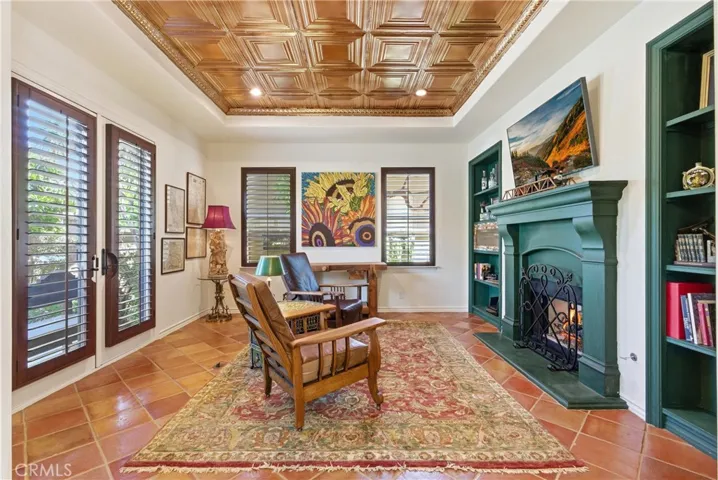 Designed for relaxation, this richly appointed room features a custom coffered ceiling, fireplace, built-in shelving, and French doors overlooking the courtyard.