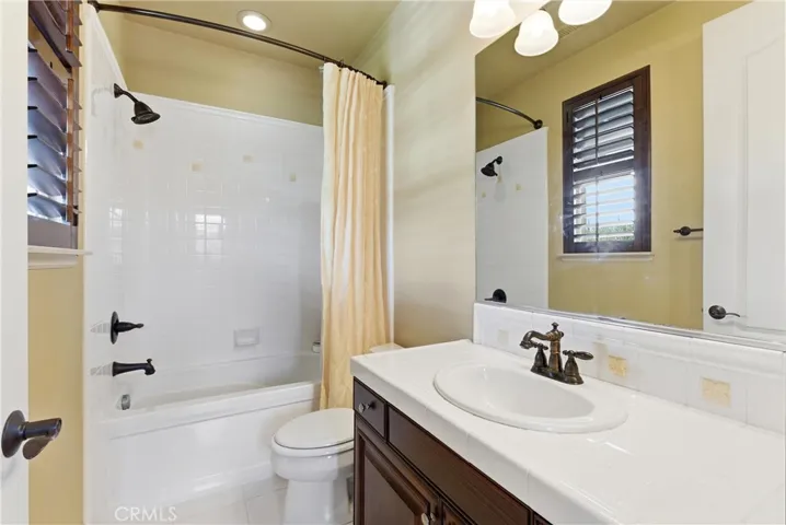 Secondary bathroom featuring a tub and shower combination, tiled countertops, and natural light.