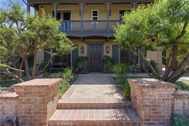 A brick-lined pathway leads through beautifully landscaped grounds to the covered front porch and grand entry, offering privacy and charm.