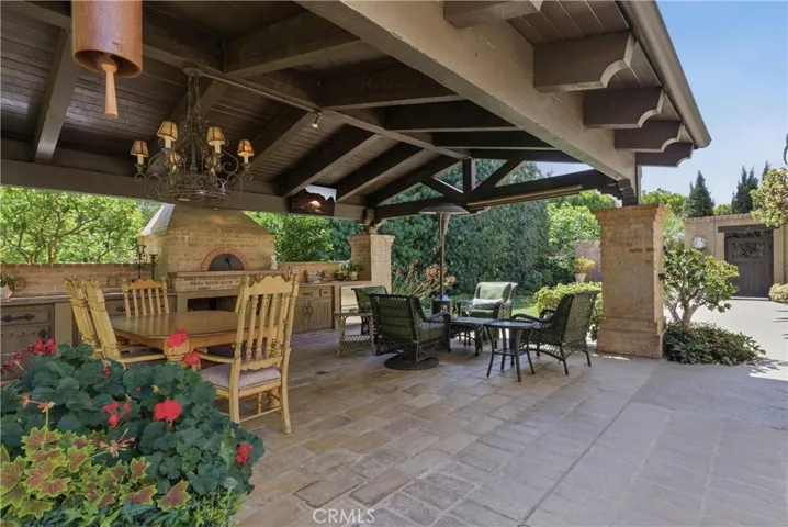 A resort-inspired outdoor pavilion features exposed beams, a dining area, lounge seating, built-in heating, and a fully equipped outdooor Mugnaini pizza oven and sink.
