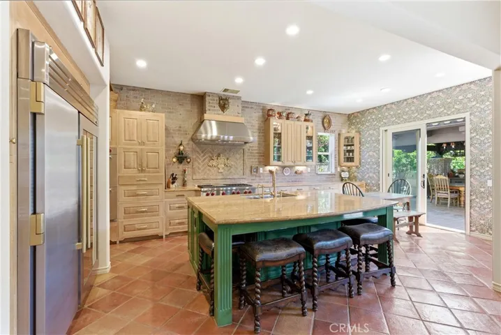 The chef's kitchen features custom cabinetry, a large center island, professional-grade appliances, brick accent walls, and authentic terracotta tile flooring.