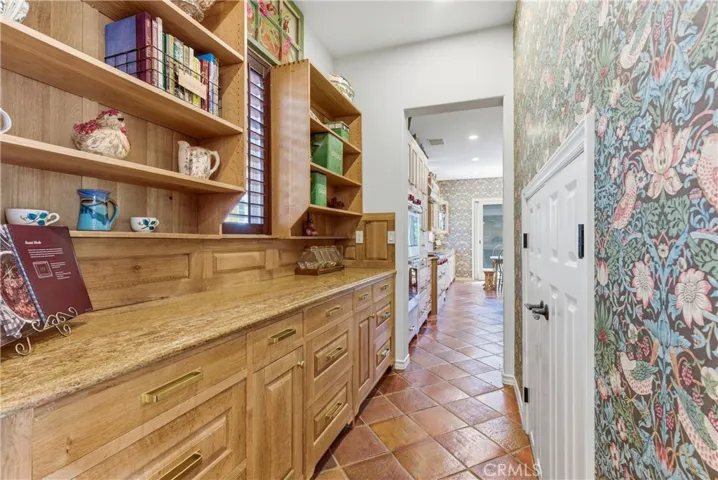 A beautifully appointed butler's pantry features custom cabinetry, extensive storage, open shelving, and generous prep space, seamlessly connecting to the kitchen