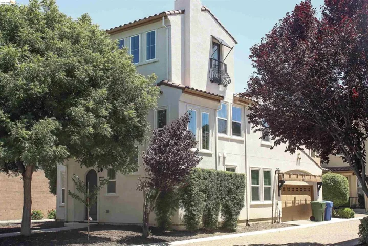 Stucco exterior featuring multiple windows, a second-story balcony with metal railing, an arched entryway, and mature landscaping