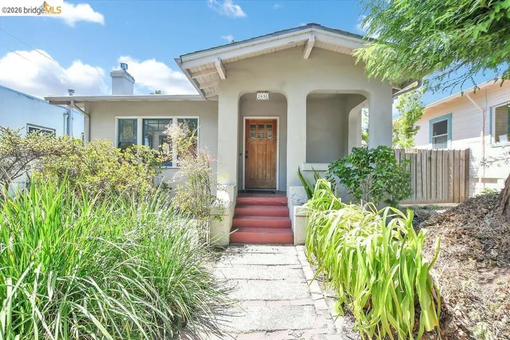 Stucco exterior with a covered front porch featuring a wood-panel entry door, red-painted concrete steps, and a stone pathway