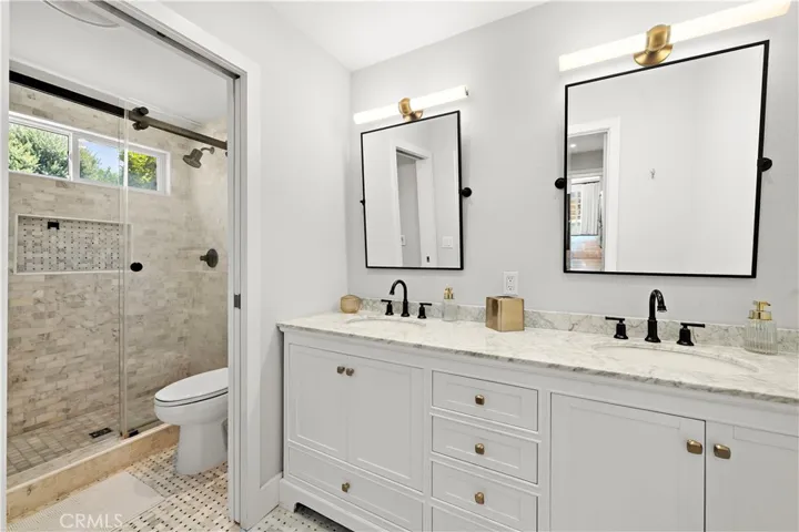 Primary bath with dual sinks, quartz countertop, and a pocket door to the walk-in shower with clear glass barn door style enclosure and designer tile surround