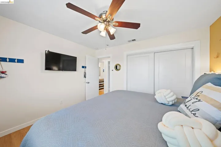 Bedroom featuring wood-finish flooring, a ceiling fan with integrated lighting, and a double-door closet with white sliding doors