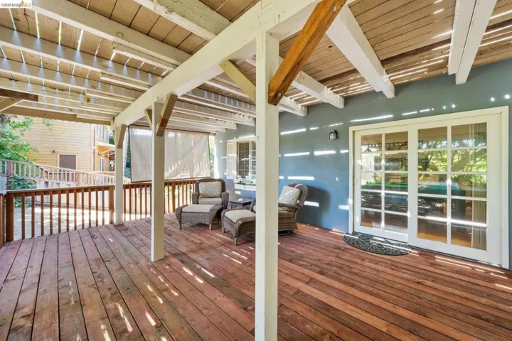 Spacious wood-finish deck with a pergola-style cover, featuring white support beams and a partial privacy screen