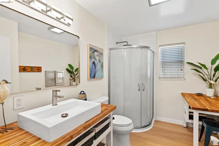 Bathroom featuring a rectangular vessel sink, wood-finish countertop, and a corner shower enclosure