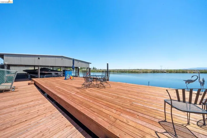 Expansive wood deck with water frontage, featuring a built-in boat house with metal siding, and a clear view of the open water