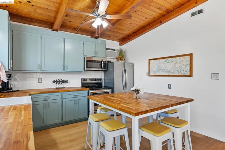 Kitchen featuring a vaulted wood-paneled ceiling with exposed beams, light blue cabinetry, butcher block countertops, and stainless steel appliances