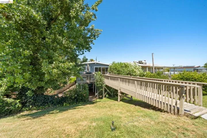 Expansive grassy yard with mature trees and a wooden ramp leading to a deck